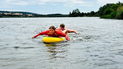 Henning Thielemeyer und Michelle Dickmann liegen bäuchlings hintereinander auf einem gelben Board im Wasser und rudern mit den Armen