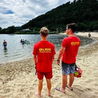 Henning Thielemeyer und Philipp Fögen stehen am Strand vom Godelheimer See und blicken auf den See, auf ihren roten T-Shirts steht auf dem Rücken "DLRG Wasserrettung"