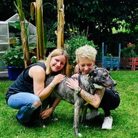 Zwei Frauen, Nadin Duberg und Susi Schmücker, hocken in einem Garten und umarmen ihre grau-weiße Hündin Wally.