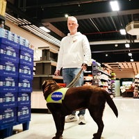 Ein Mann steht im Supermarkt. An der Leine hält er einen braunen Labrador.