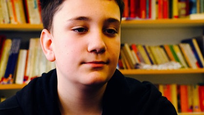 Portraitfoto eines Schülers beim Rap-Workshop. Hinter ihm befindet sich ein Bücherregal.