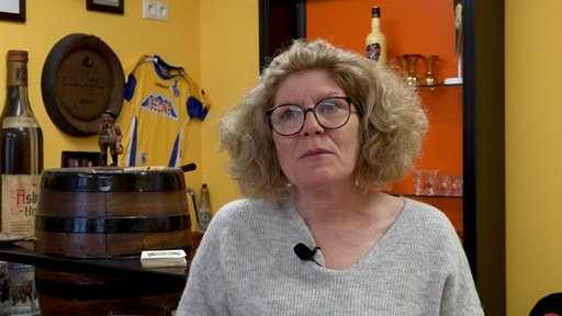 Portraitfoto von Heike Petzold, blonde Frau mit Locken und Brille steht in Kneipe.