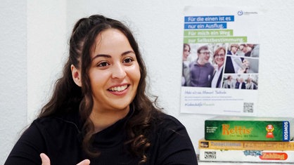 Eine junge Frau sitzt in einem Raum und schaut links an der Kamera vorbei.