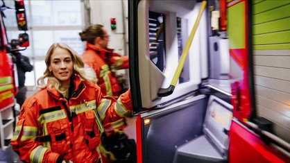 Eine Frau springt in ein Feuerwehrauto und blickt an der Kamera vorbei