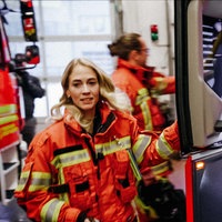 Eine Frau springt in ein Feuerwehrauto und blickt an der Kamera vorbei