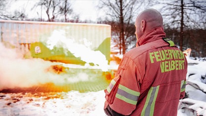 Ein Mann steht vor einer grellen Flamme an einem Container