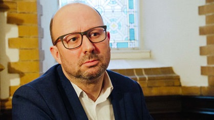 Pfarrer Joachim Hall aus der evangelischen Gemeinde Elberfeld-Nord in Wuppertal steht vor einem bunten Kirchenfenster
