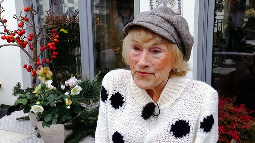 Edith Clemes trägt einen Wollpullover und eine Mütze. Sie steht auf ihrer Terrasse.