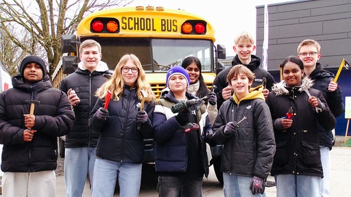 Schülerinnen und Schüler stehen vor einem gelben alten US-Schulbus.