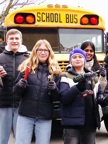 Schülerinnen und Schüler stehen vor einem gelben alten US-Schulbus.