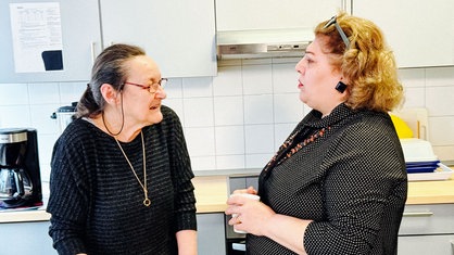 Margret Wagner und Tooran Tammasebi stehen mit Tassen in den Händen gemeinsam in der Küche.