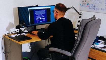 Peter Klim sitzt an einem Schreibtisch und spielt am Computer.