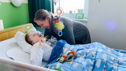 Eine Frau schaut einen Jungen, der im Bett liegt, liebevoll an.