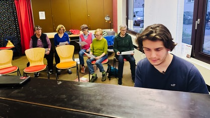 Senioren sitzen in Stuhlreihen hinter einem Flügel und singen gemeinsam.