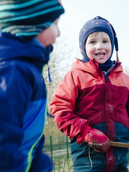 Zwei spielende Kinder in bunten Jacken, eines lacht in die Kamera