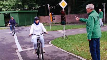 Eine Frau fährt Fahrrad. Ein Übungsleiter zeigt ihr einen Daumen nach oben.
