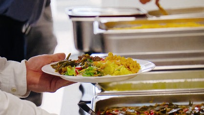 Ein mit verschiedenen Speisen gefüllter Teller vor einem Buffet. 