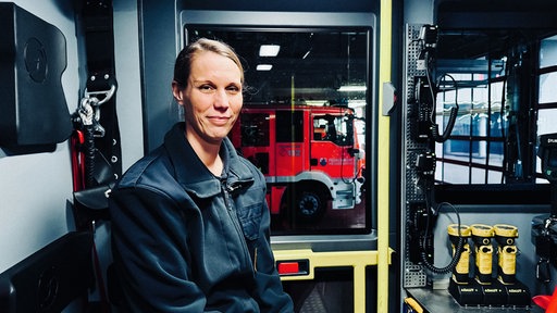 Katharina Kluge im Portrait in der Garage des Feuerwehrgebäudes. Im Hintergrund ein Feuerwehrfahrzeug.