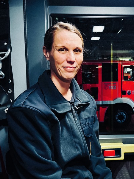 Katharina Kluge im Portrait in der Garage des Feuerwehrgebäudes. Im Hintergrund ein Feuerwehrfahrzeug.