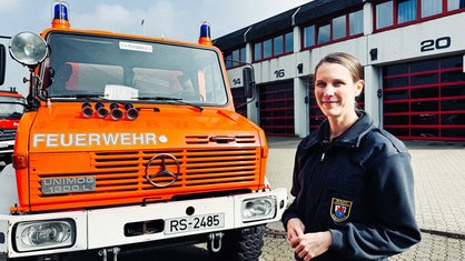 Katharina Kluge steht rechts vor einem Einsatz-Lastwagen im Innenhof der Feuerwehrwache.