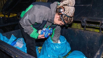 Ein Mann sucht in einem vollen Müllcontainer an einem Supermarkt nach Lebensmitteln