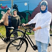 Drei Frauen mit Helm stehen neben zwei Fahrrädern auf der Straße.