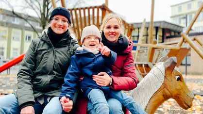 Die Mütter Lisa und Anna-Lena Heidemann sitzen zusammen mit ihrem dreijährigen Sohn Joris auf einem Spielplatz