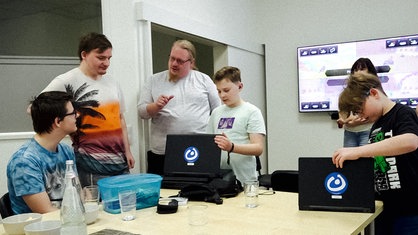 Falk Sommerfeld spricht mit einer Gruppe von Kindern und Jugendlichen. Zwei davon begutachten Laptops.