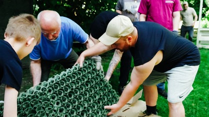 Walat Nargili hebt mit zwei weiteren Personen ein Gartendekoelement an