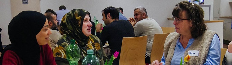 Verschiedene Menschen sitzen an einem Tisch und essen gemeinsam.