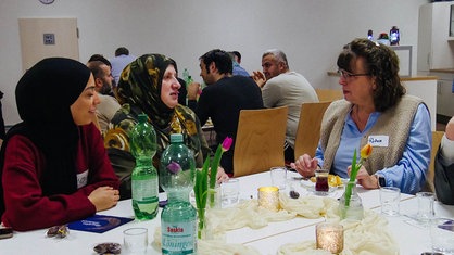 Verschiedene Menschen sitzen an einem Tisch und essen gemeinsam.