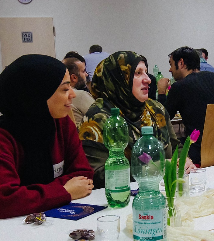 Verschiedene Menschen sitzen an einem Tisch und essen gemeinsam.