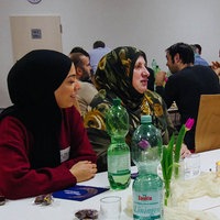 Verschiedene Menschen sitzen an einem Tisch und essen gemeinsam.