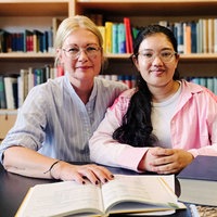 Zwei Frauen, die vor einem aufgeschlagenen Buch sitzen.