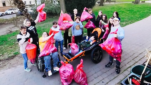 Eine Gruppe von Menschen hebt gesammelten Müll in pinken Tüten in die Luft.