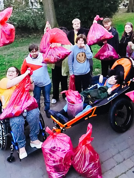 Eine Gruppe von Menschen hebt gesammelten Müll in pinken Tüten in die Luft.