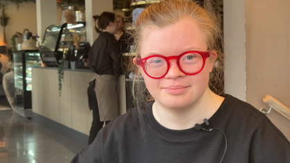 Christine trägt eine große rote Brille und lächelt leicht in die Kamera.