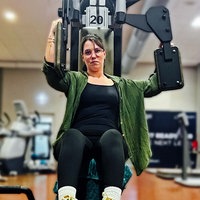 Angelina Schirmer sitzt auf einem Butterfly-Gerät im Fitnessstudio. Ihren rechten Arm am Gerät drückt sie nach vorne, der linke bleibt hinten.