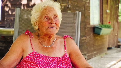Die 86-jährige Christel Varga sitzt in einem rosa Kleid in einem Gartenstuhl.