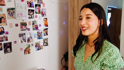 Ghada Abbassis vor einer Wand mit einigen Fotos. Sie trägt ein grünes Kleid und lächelt