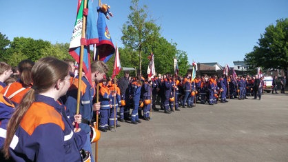 In Borken stehen Gruppen von Jugendfeuerwehrleuten in blauer Uniform und mit Fahnen nebeneinander.