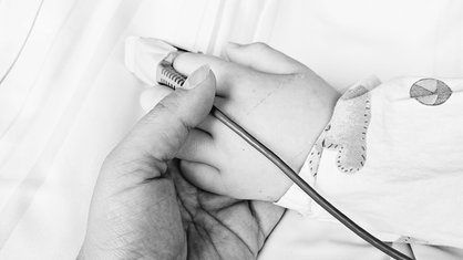 Die Hand einer Mutter hält die Hand ihres Sohnes, die mit Kabeln im Krankenhaus versehen ist.