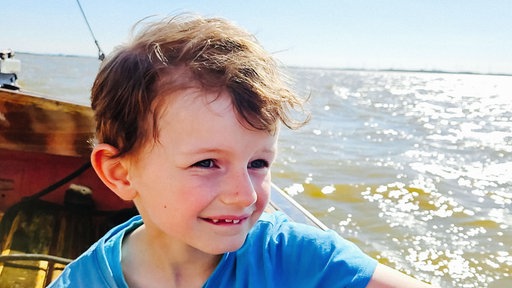 Porträt eines kleinen Jungen, der auf einem Schiff sitzend über das Meer fährt.