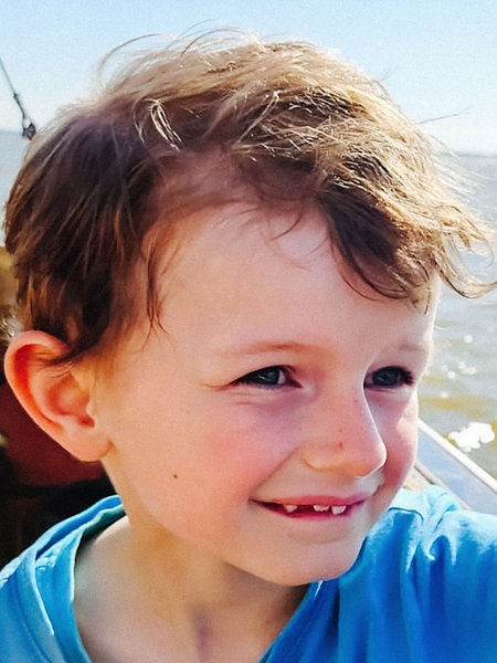 Porträt eines kleinen Jungen, der auf einem Schiff sitzend über das Meer fährt.