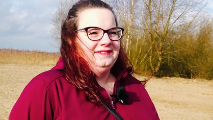 Porträt einer Frau, die draußen vor Bäumen steht. 