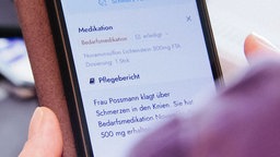 Nahaufnahme eines in einer Hand gehaltenen Smartphones, das eine Pflegedokumentation auf dem Display zeigt.