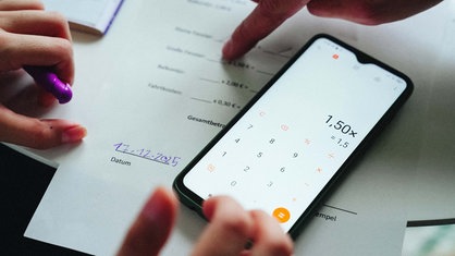Auf einem gedruckten Abrechnungsbogen liegt ein Smartphone, auf dem der Taschenrechner geöffnet ist.