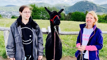 Elke und Jenny stehen mit einem Alpaka auf einer Weide.