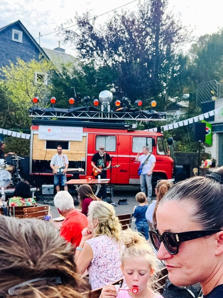 Eine vierköpfige Band steht vor einem alten Feuerwehrauto und spielt ein Konzert.