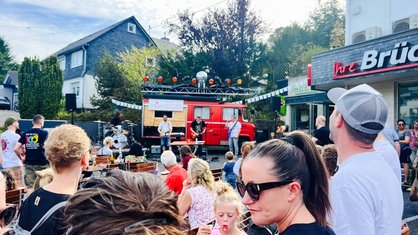 Eine vierköpfige Band steht vor einem alten Feuerwehrauto und spielt ein Konzert.